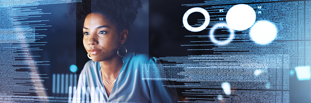 Woman sits in front of computer. Her screen is visible. She is coding.